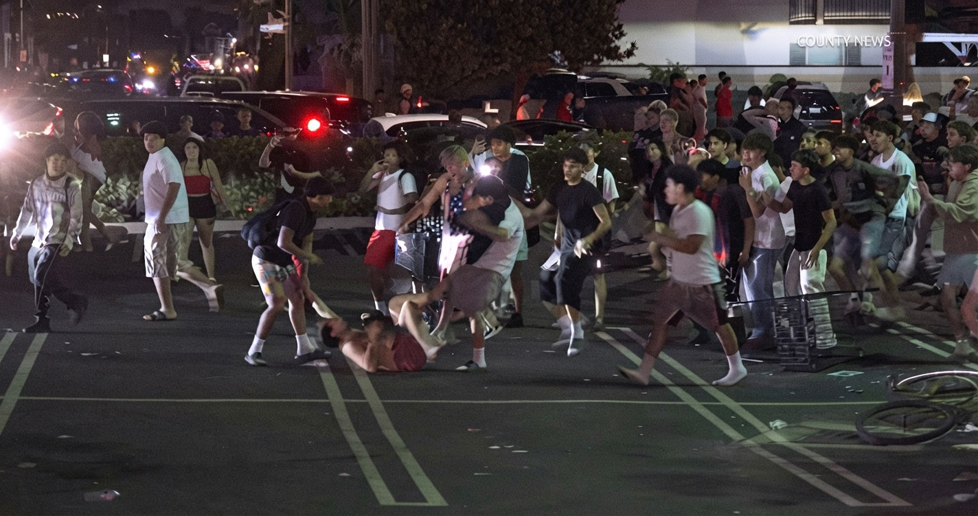 Nighttime street scene with a large crowd of people running; one person lies on the ground while others rush past.