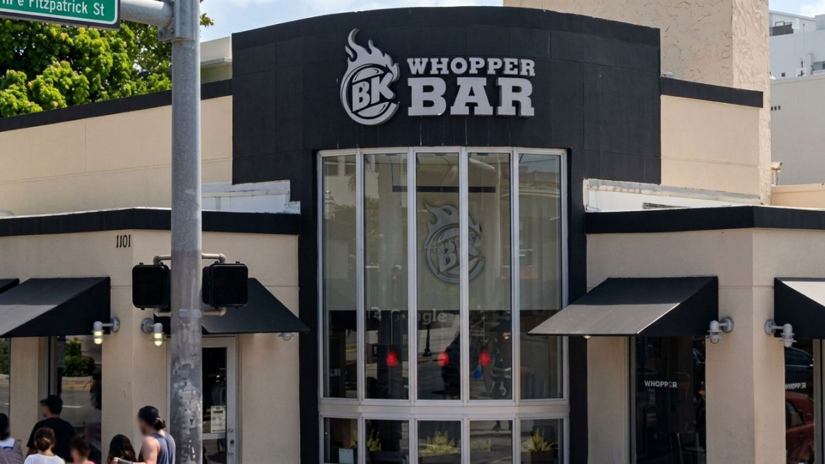 Whopper Bar storefront with large curved glass windows, bold BK logo, and pedestrians nearby on the sidewalk.