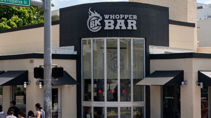 Whopper Bar storefront with large curved glass windows, bold BK logo, and pedestrians nearby on the sidewalk.
