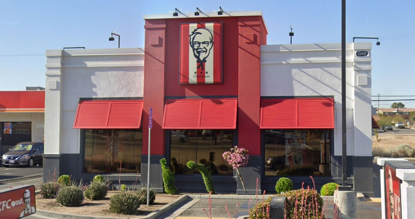 Front view of a KFC restaurant with red awnings, large windows, and a Colonial Sanders sign mounted on a red tower.